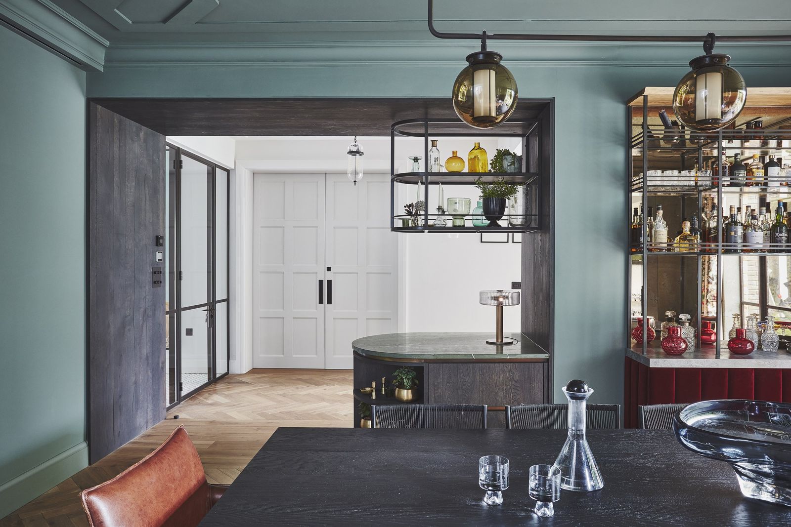 Home bar in dark joinery beside a green-panelled sitting room