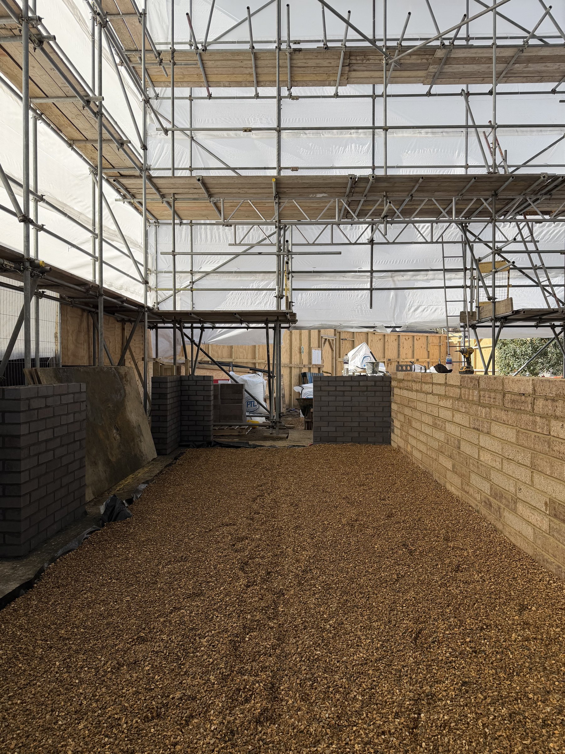 Brick plinth walls rising inside a fully sheeted scaffold enclosure