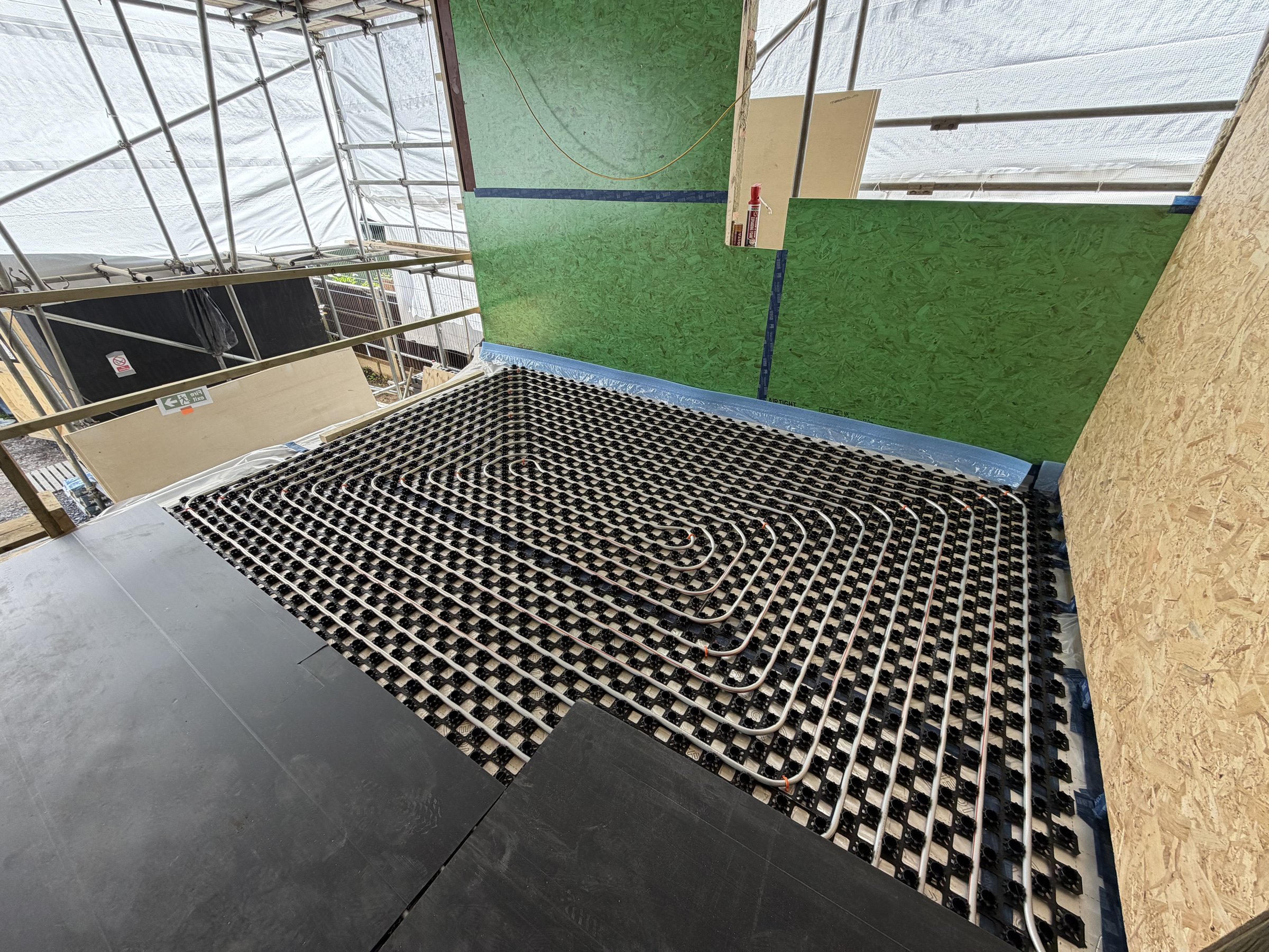 Underfloor heating pipework clipped over castellated overlay panels