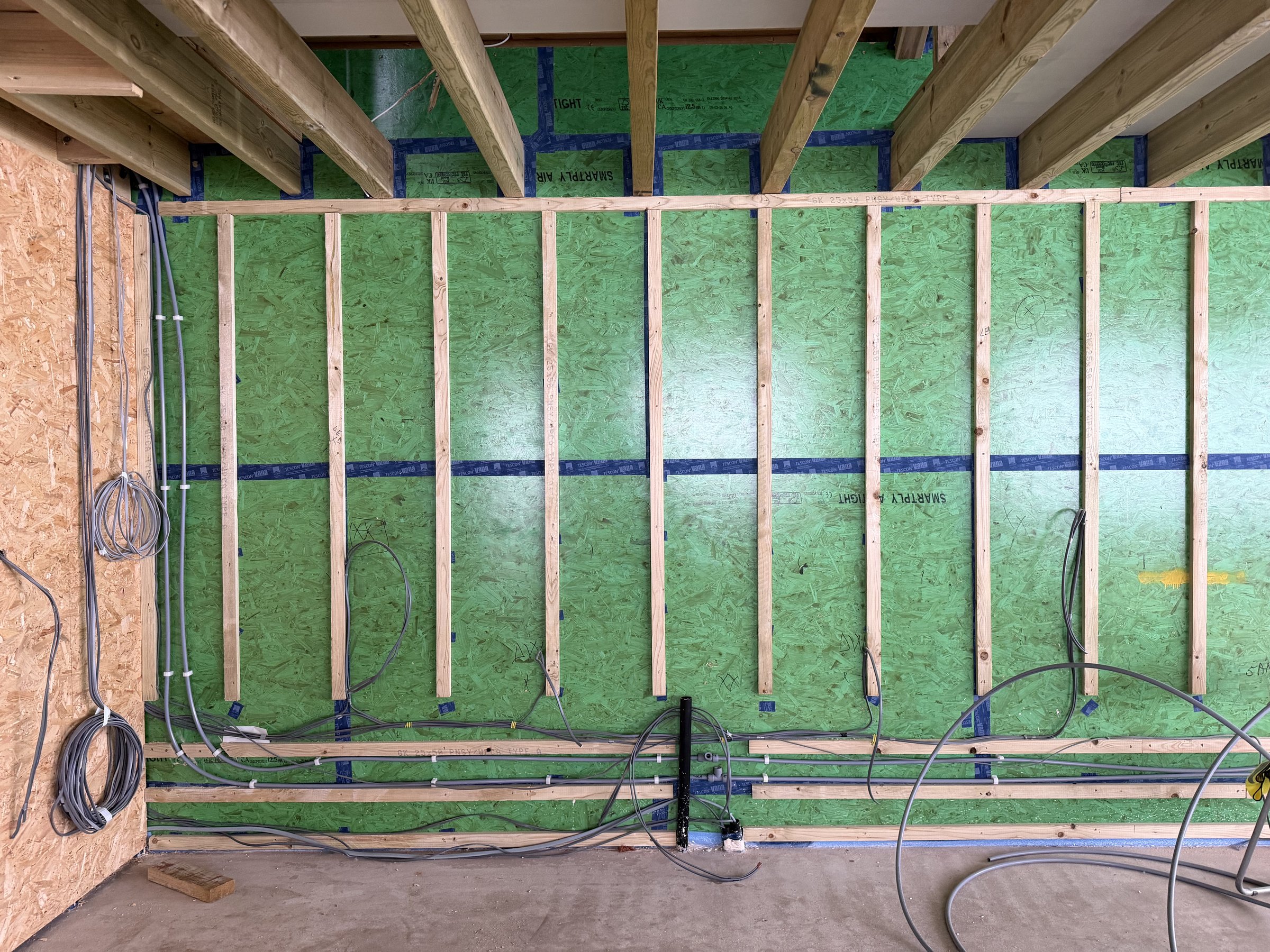 Airtight sheathing taped at every joint with a tape collar around each ceiling joist, first-fix cables clipped to battens below