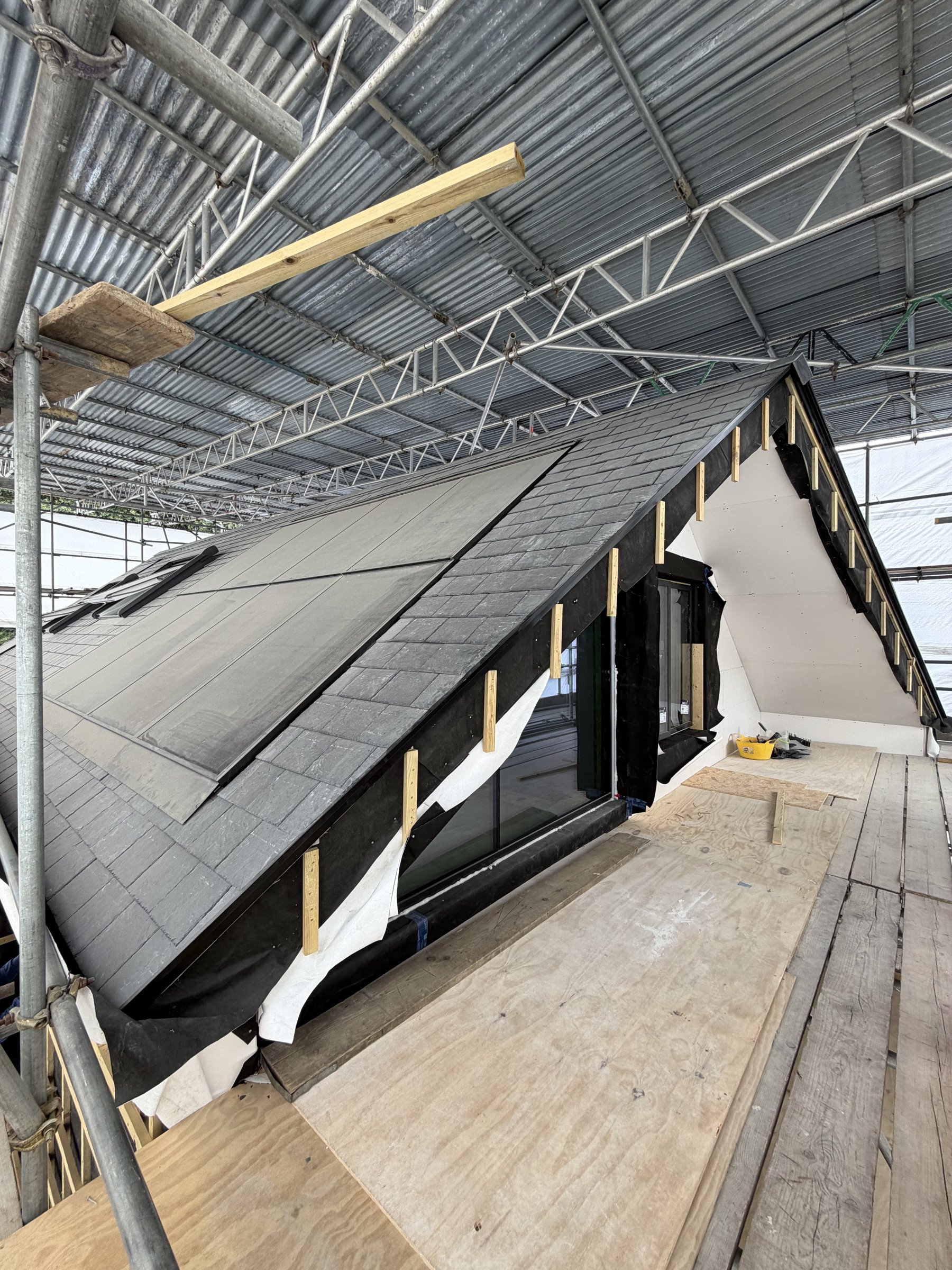 Black House slate roof with solar panels and rooflights set into the roof plane, beneath the scaffold canopy