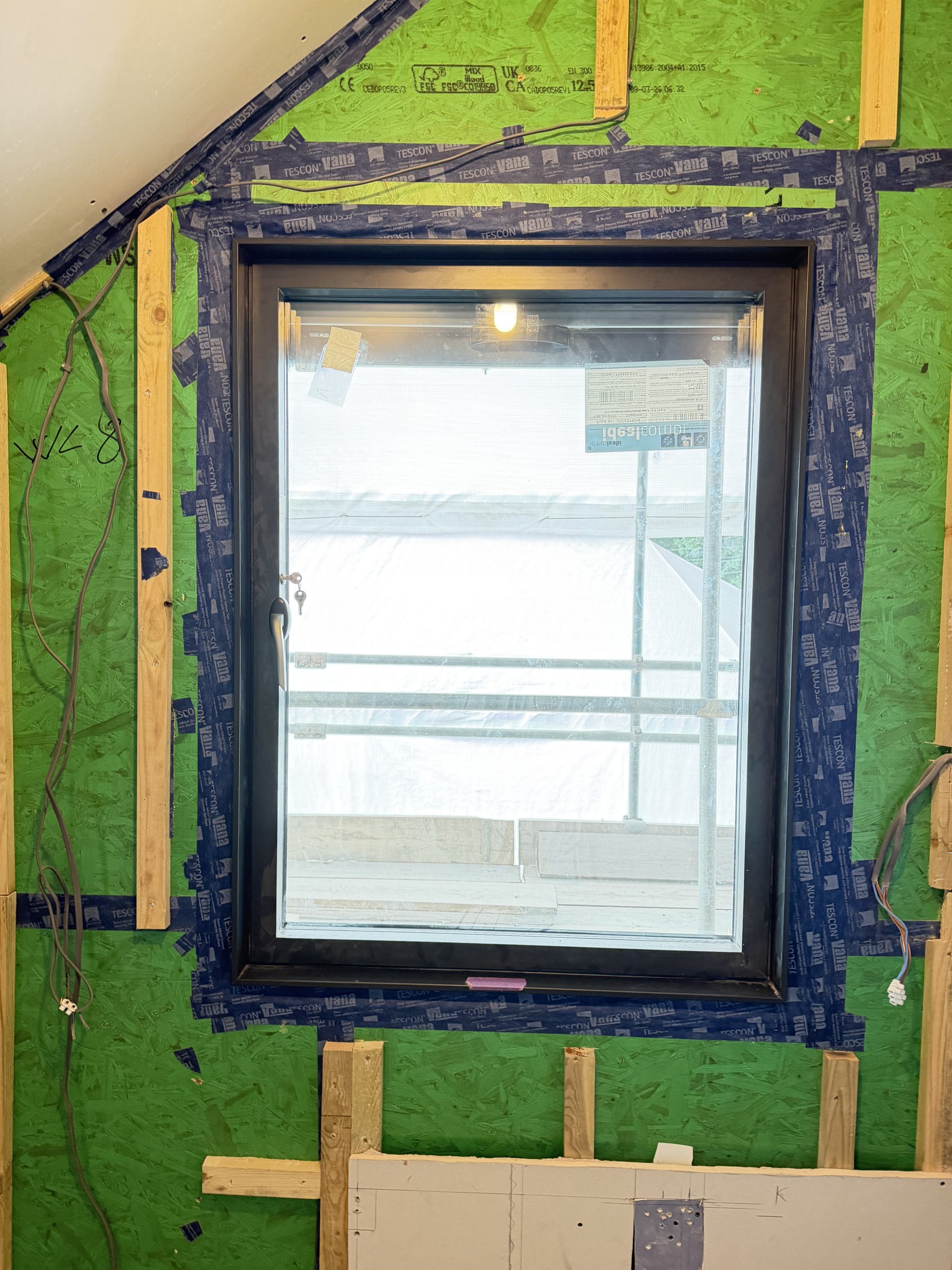 Black aluminium window frame taped to the green airtight board on all four sides at Black House