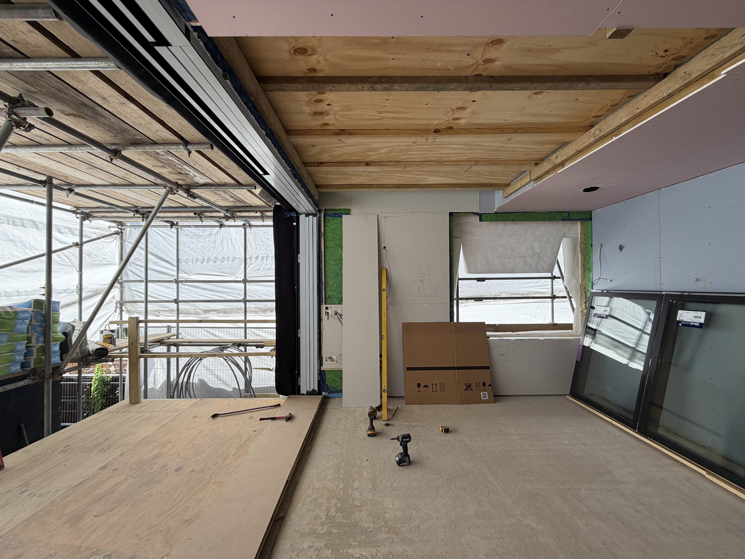The sliding door frame installed, the opening clear to the plywood-decked rear terrace, exposed ceiling joists over the room