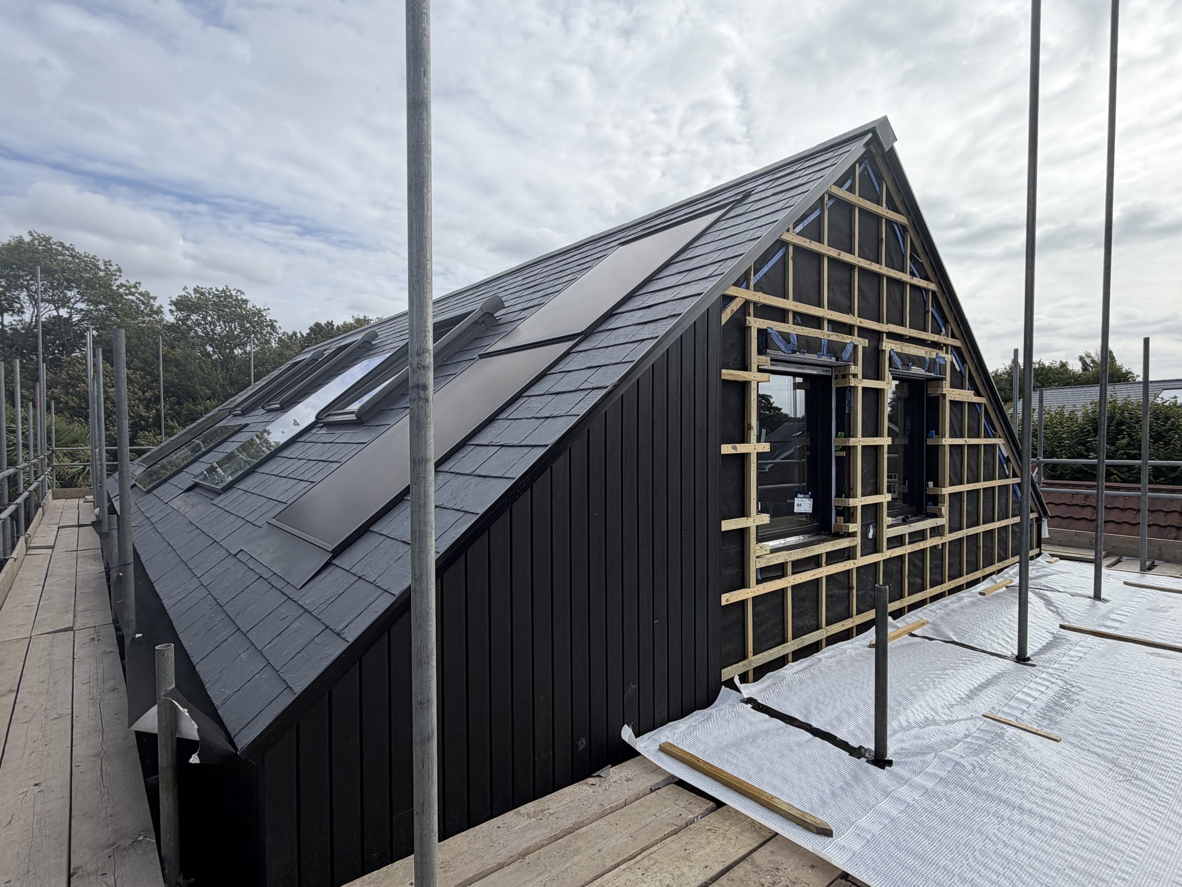 The slated roof in daylight with flush solar panels and rooflights, black vertical timber cladding to the side wall and the gable battened out around two windows