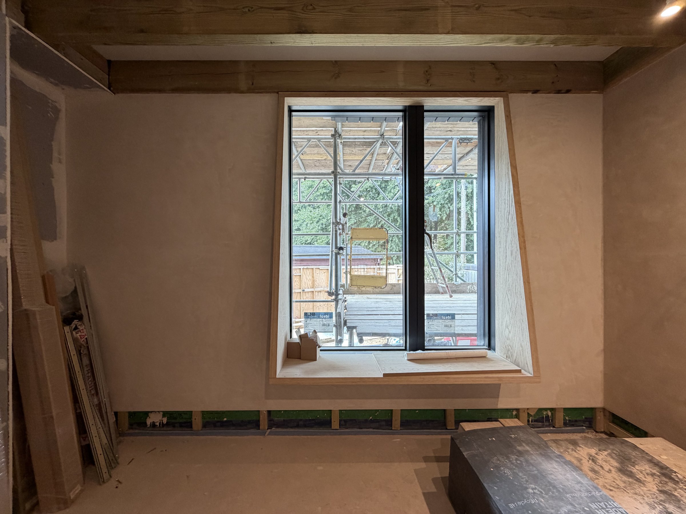 A window with splayed oak-lined reveals and a deep oak sill forming a window seat, set in lime-plastered walls under exposed timber joists