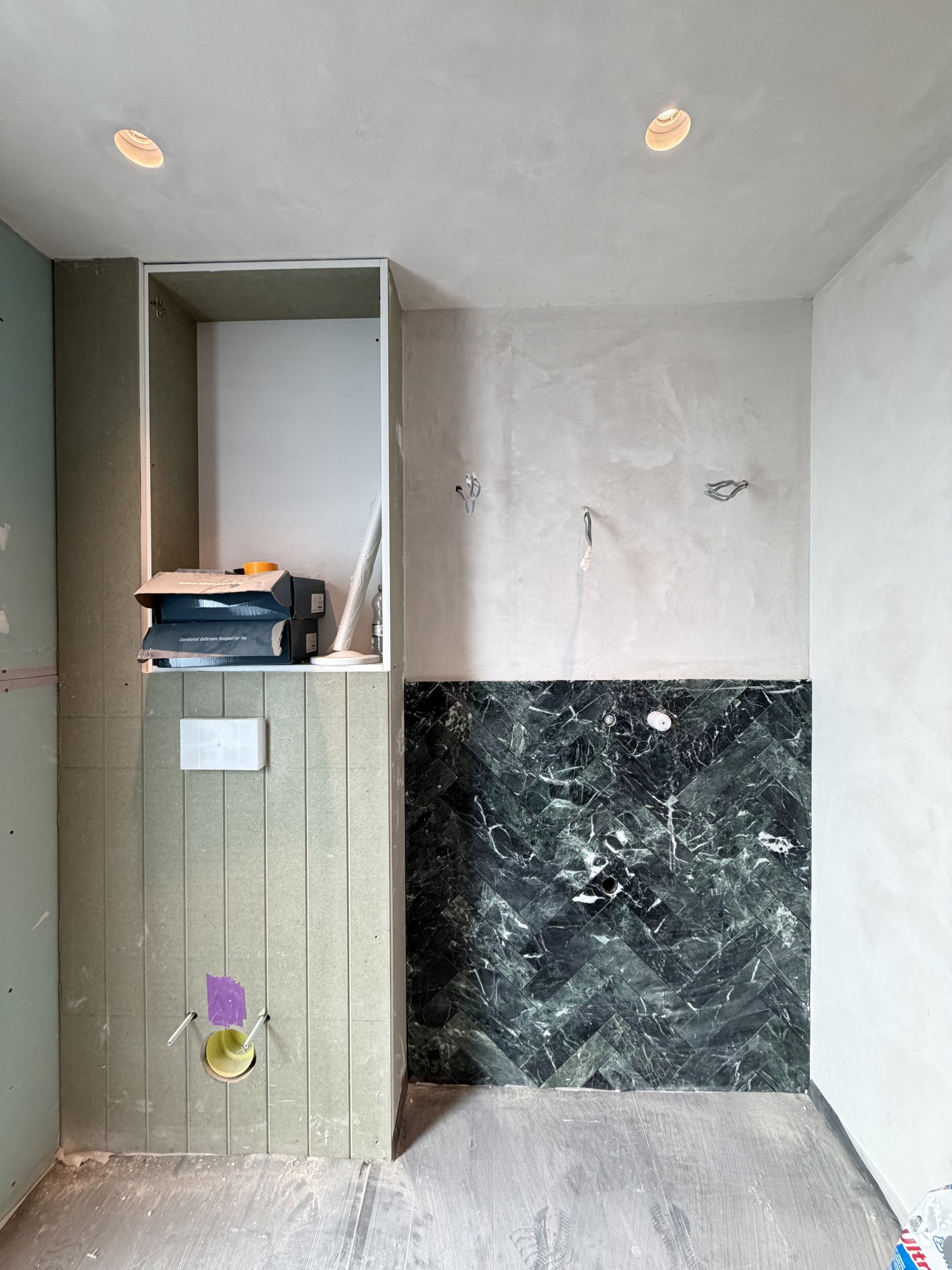 Ground floor cloakroom with green honed marble laid in herringbone behind the vanity, lime-plastered walls and ceiling above, and a V-groove panelled box for the WC frame