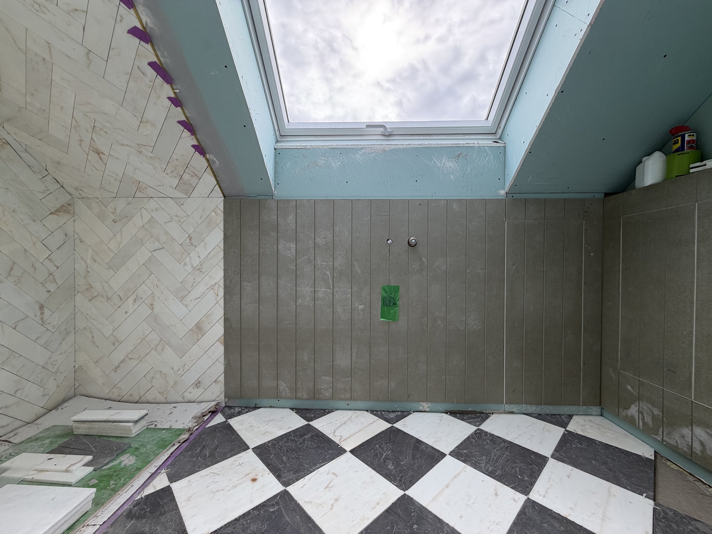 Loft bathroom with herringbone marble to the shower and the sloping ceiling, a black and white marble floor laid on the diagonal, V-groove panelling and a rooflight