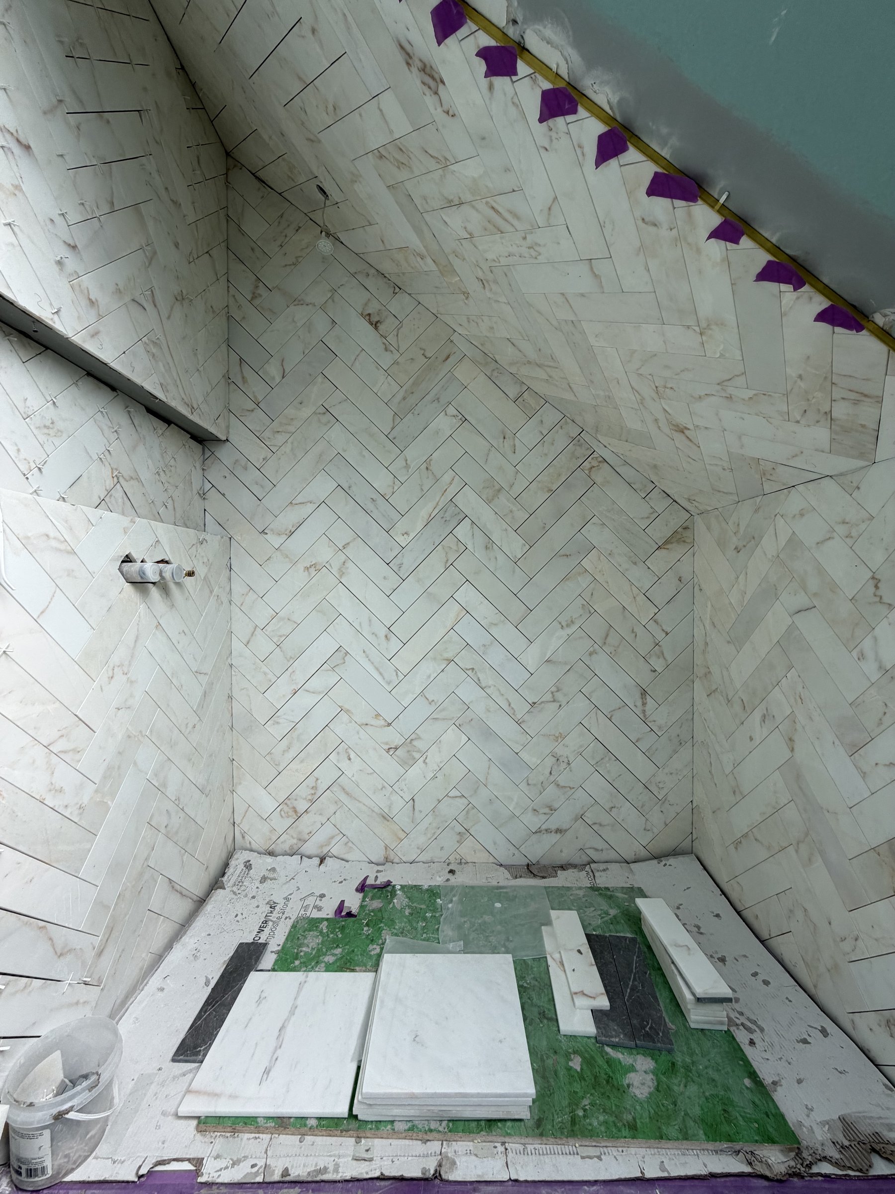 Inside the loft shower, herringbone marble running from the wall onto the sloping ceiling, floor tiles stacked on the green waterproofing
