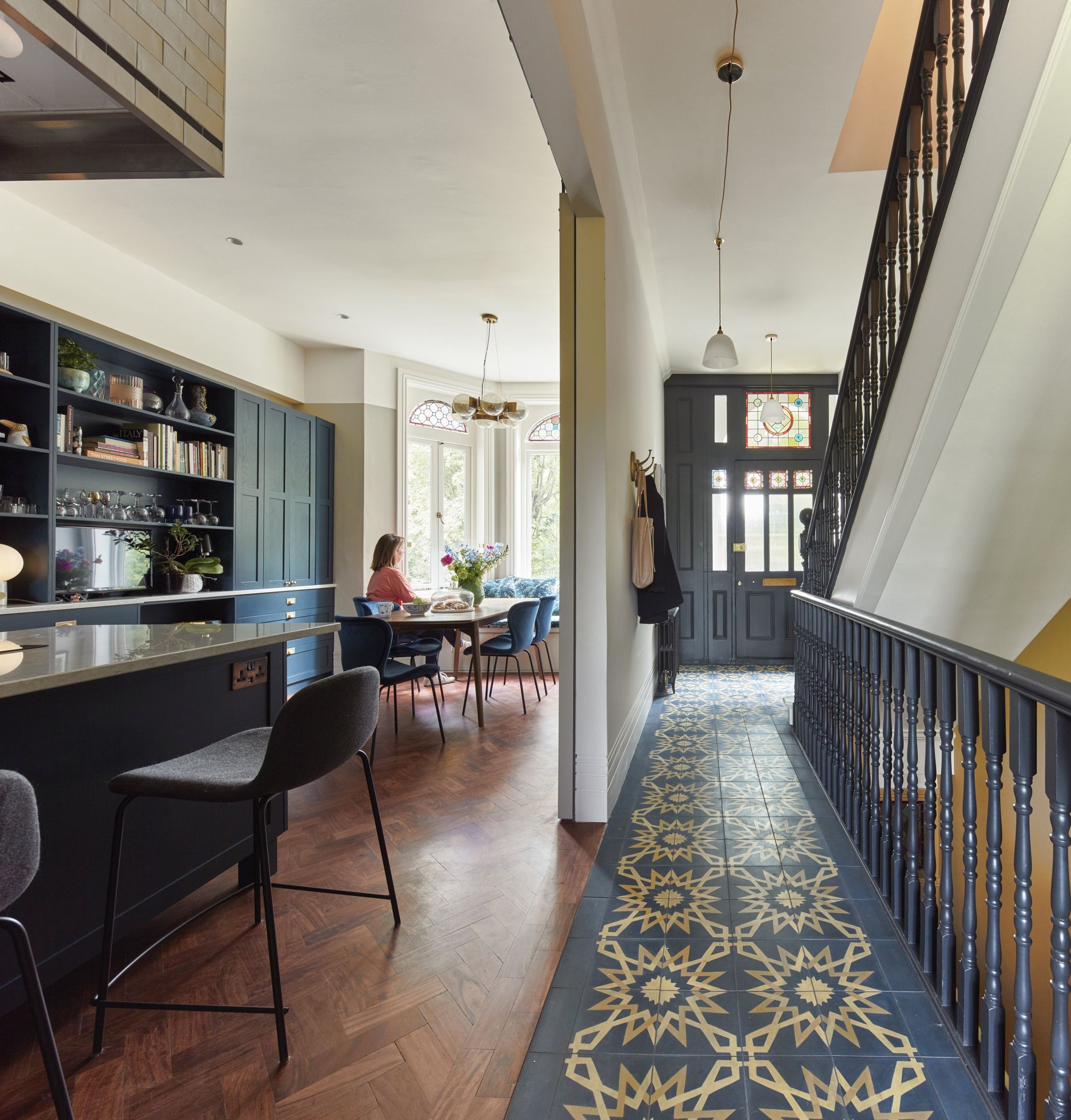 Hallway with patterned runner, dark balustrade, and view to the kitchen