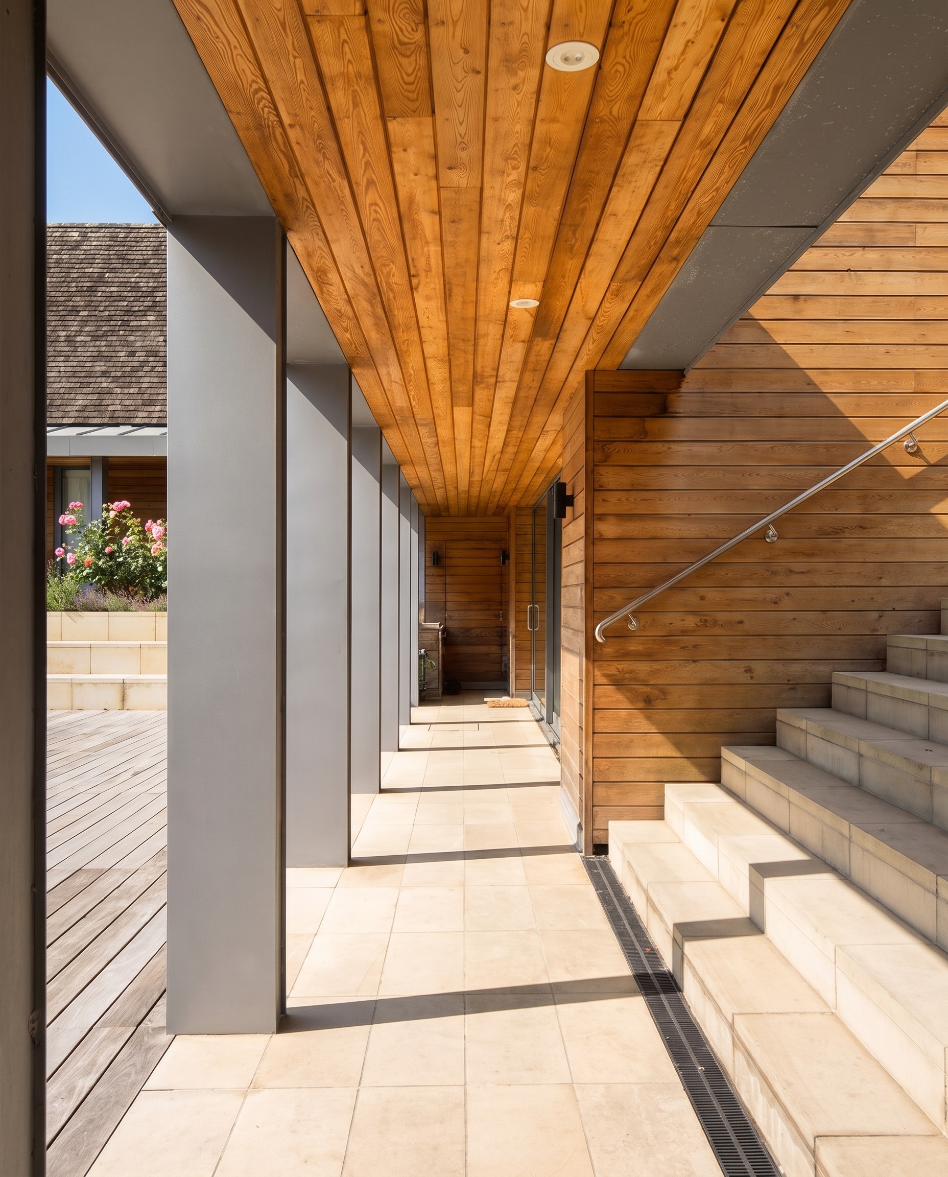Covered walkway with timber-lined soffit beside an external stone stair