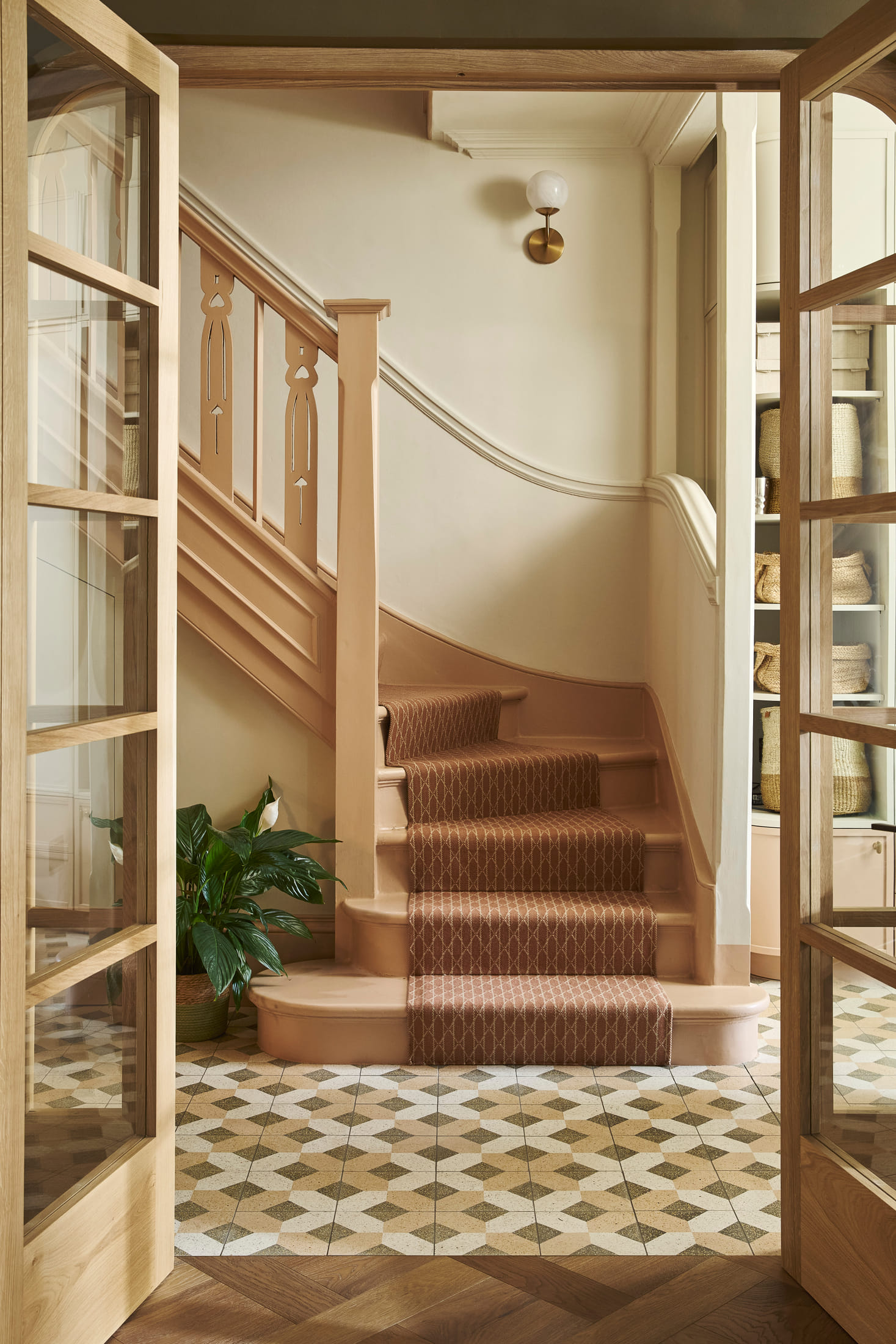 Restored staircase with a patterned runner over a geometric tiled floor, seen through the oak doors