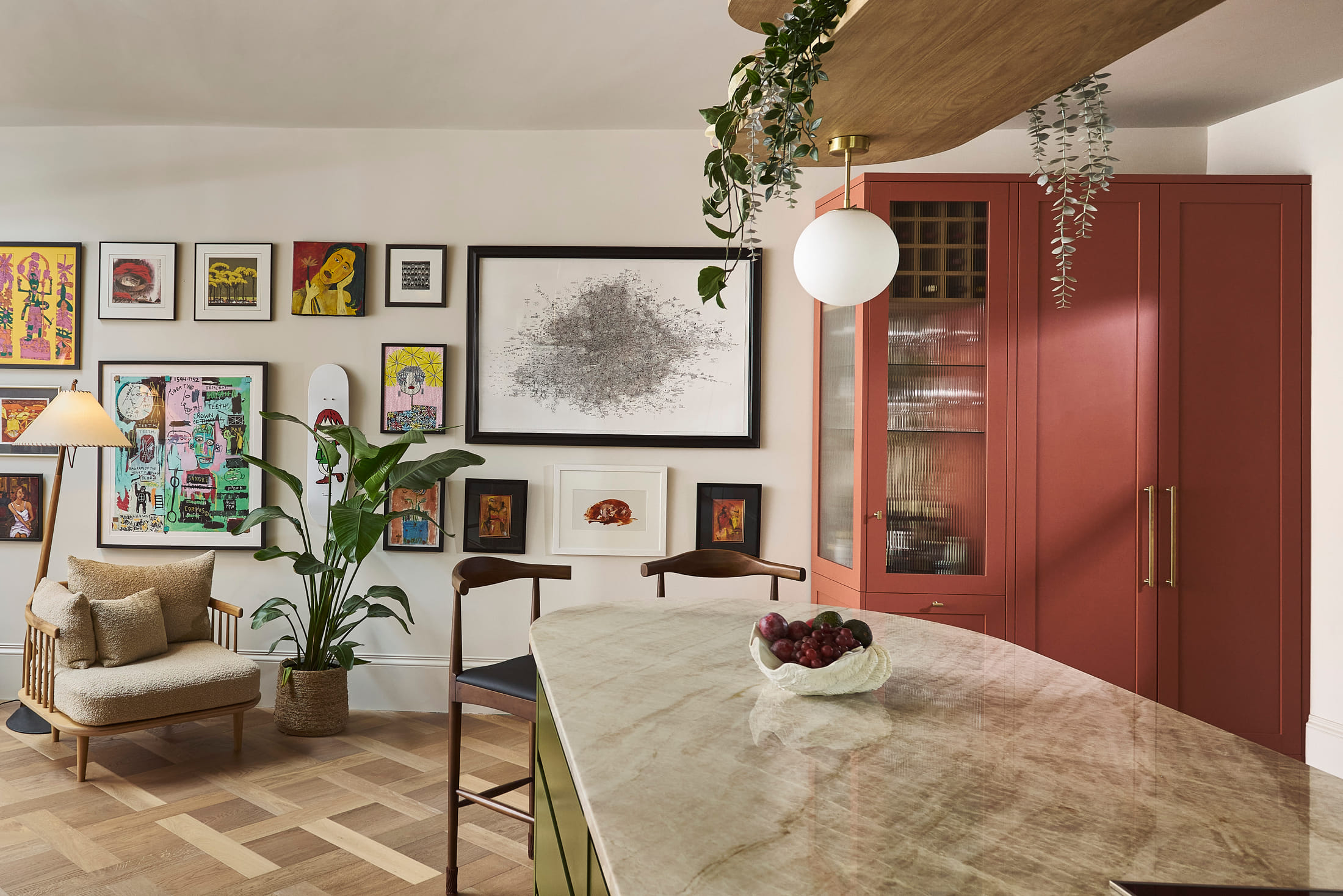 Stone-topped island in front of tall oxblood cabinets and a hung wall of framed art