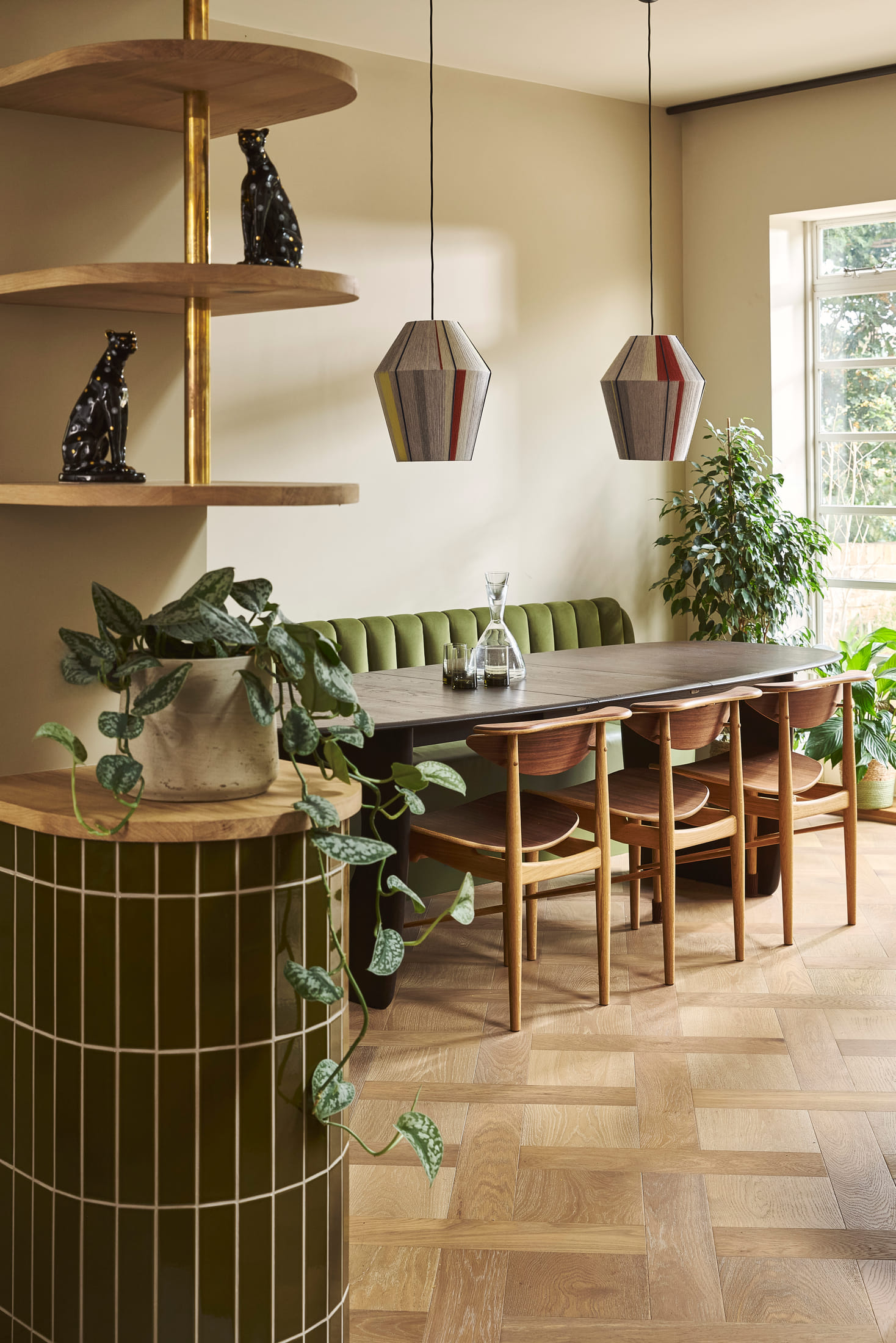 Green glazed tile island end below open shelving in oak and brass