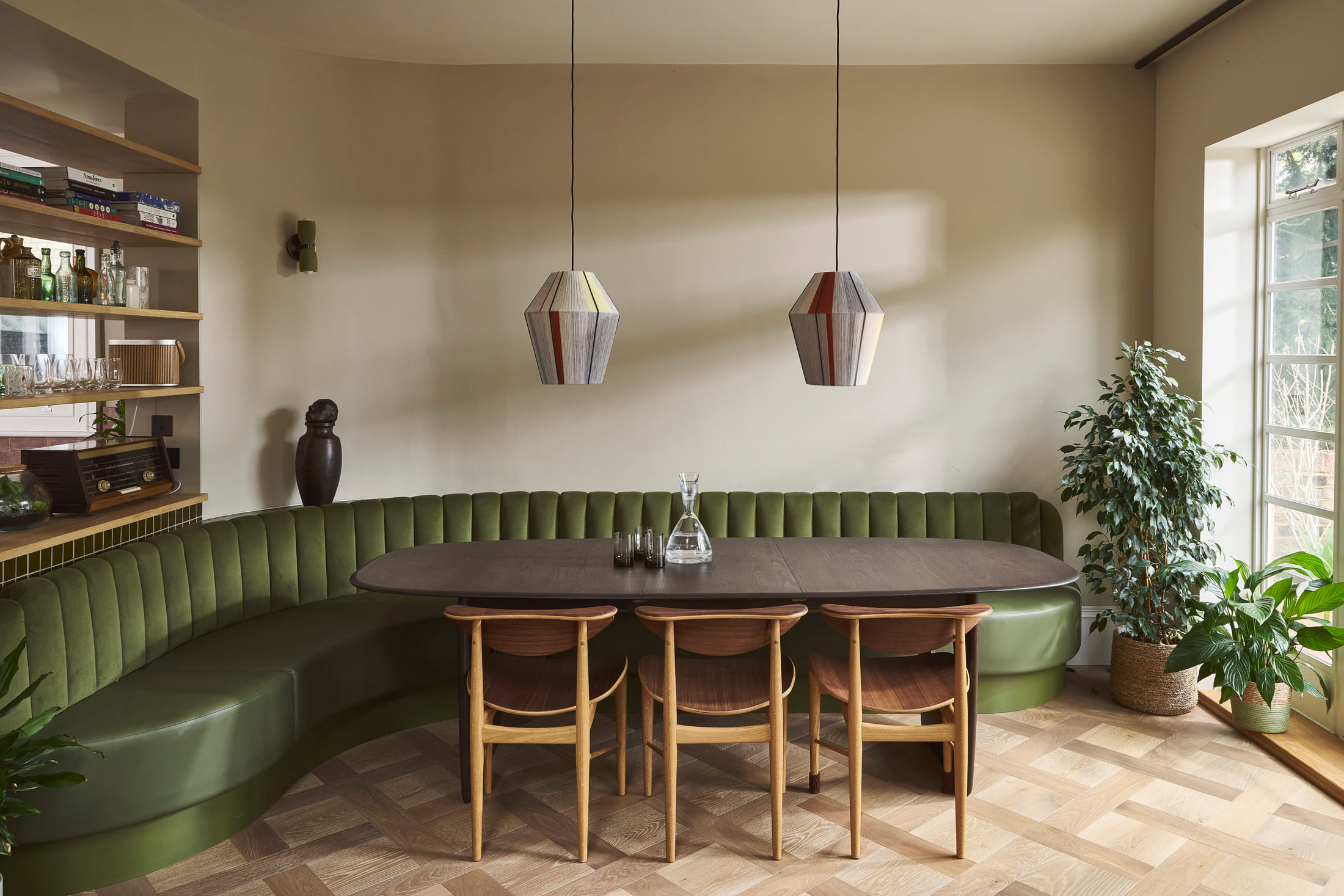 Curved green velvet banquette around the dining table under a pair of pendants