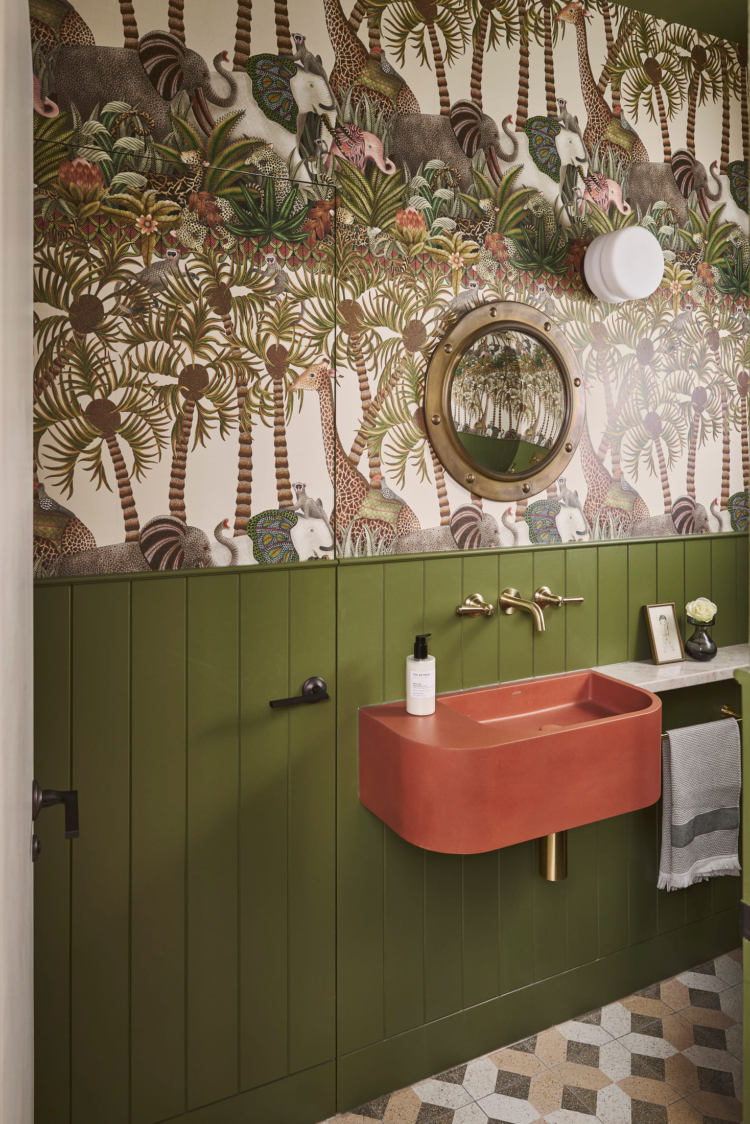 Boot room in green panelling with a terracotta basin and patterned floor tiles