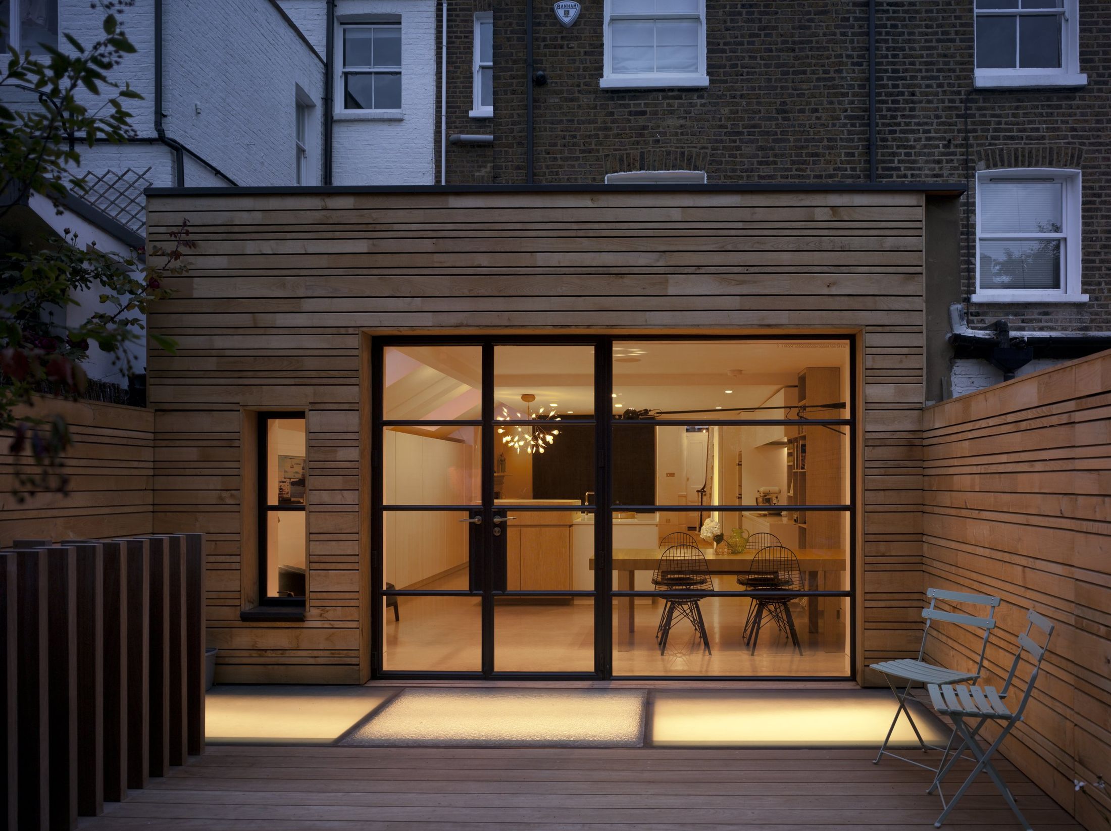 Timber-clad rear extension glowing at dusk with steel-framed glazing