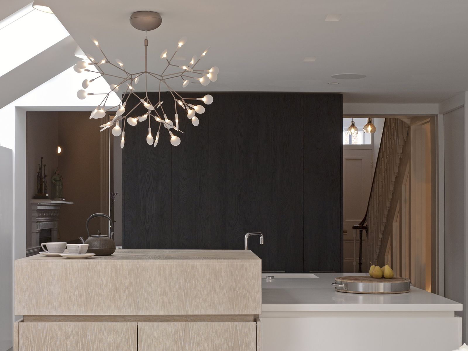 Pale kitchen with island and dark timber stair beyond