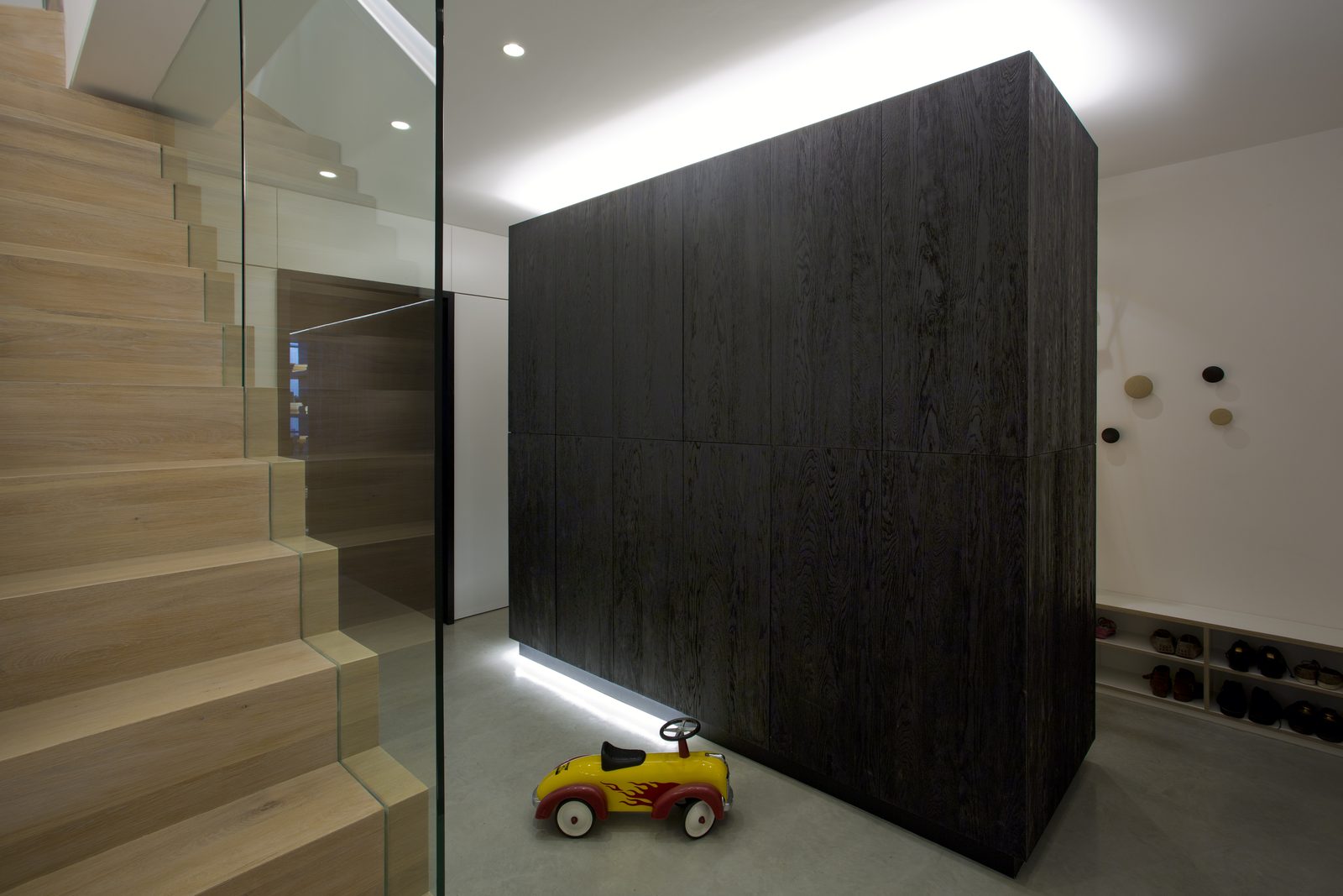 Blackened timber box at the foot of the oak stair, lit from below