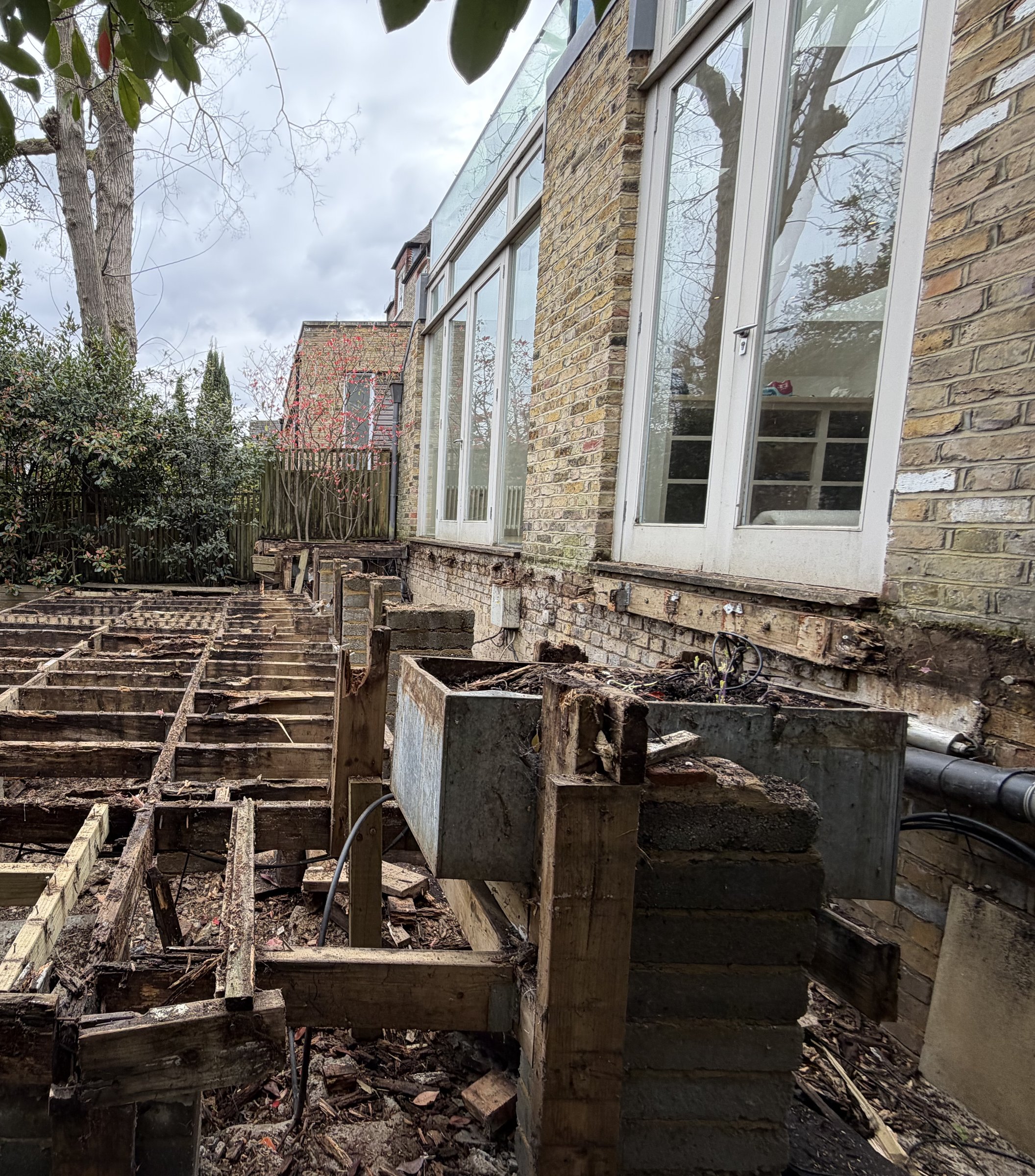The tiered deck stripped back to its joist grid along the rear of the house, rotten joist ends exposed