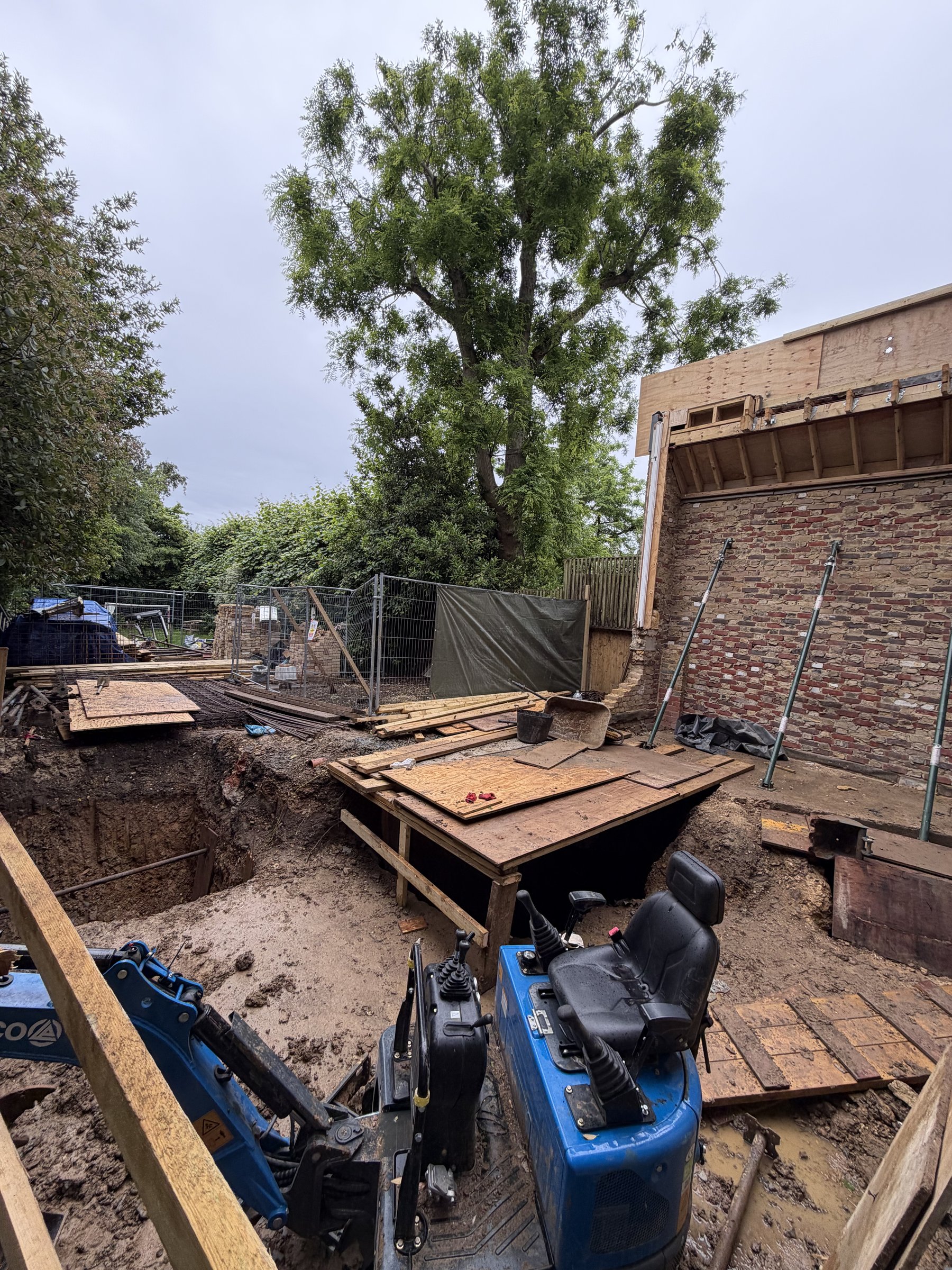 The rear of the house propped on shores while the basement is dug beneath, new flat roof structure above