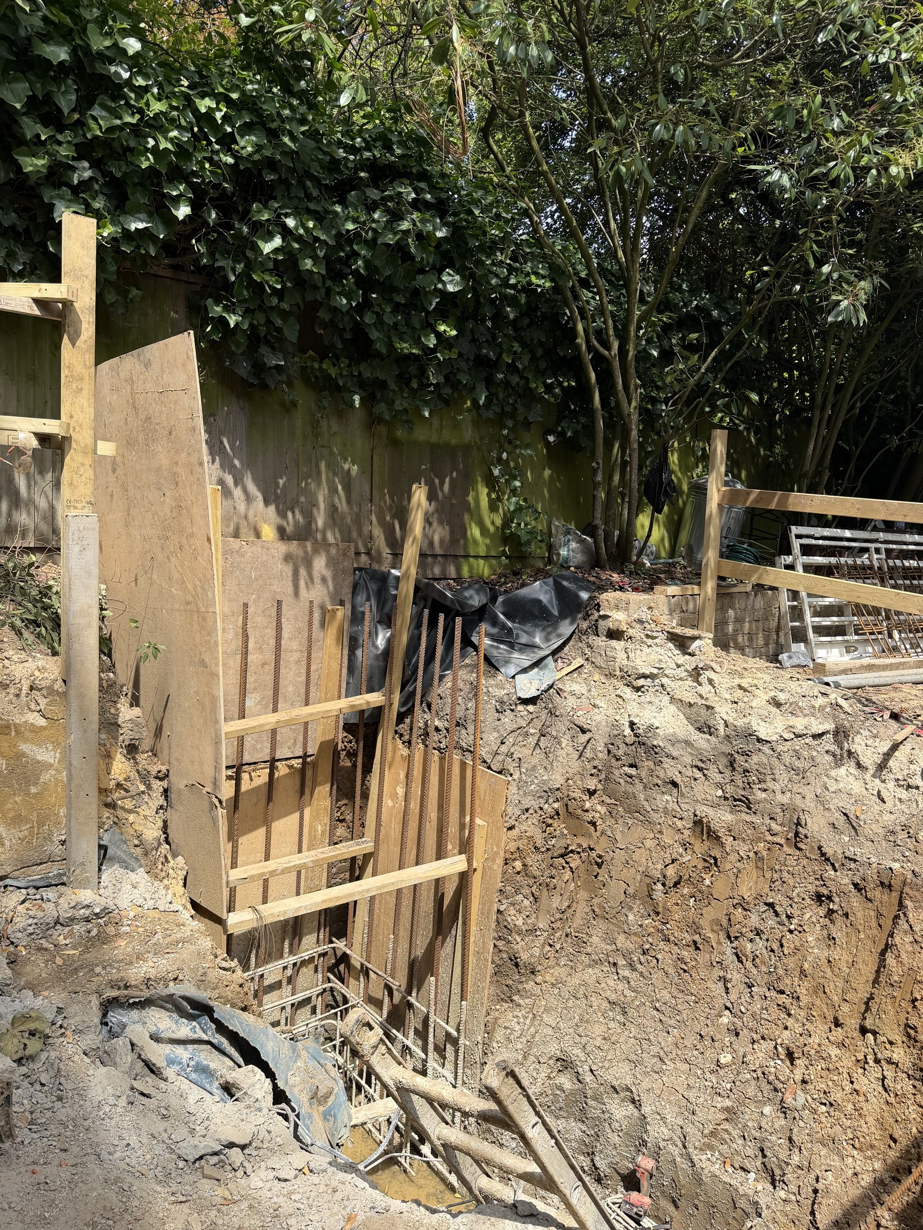 Retaining wall reinforcement fixed against plywood shutters at the garden boundary, damp proof membrane behind