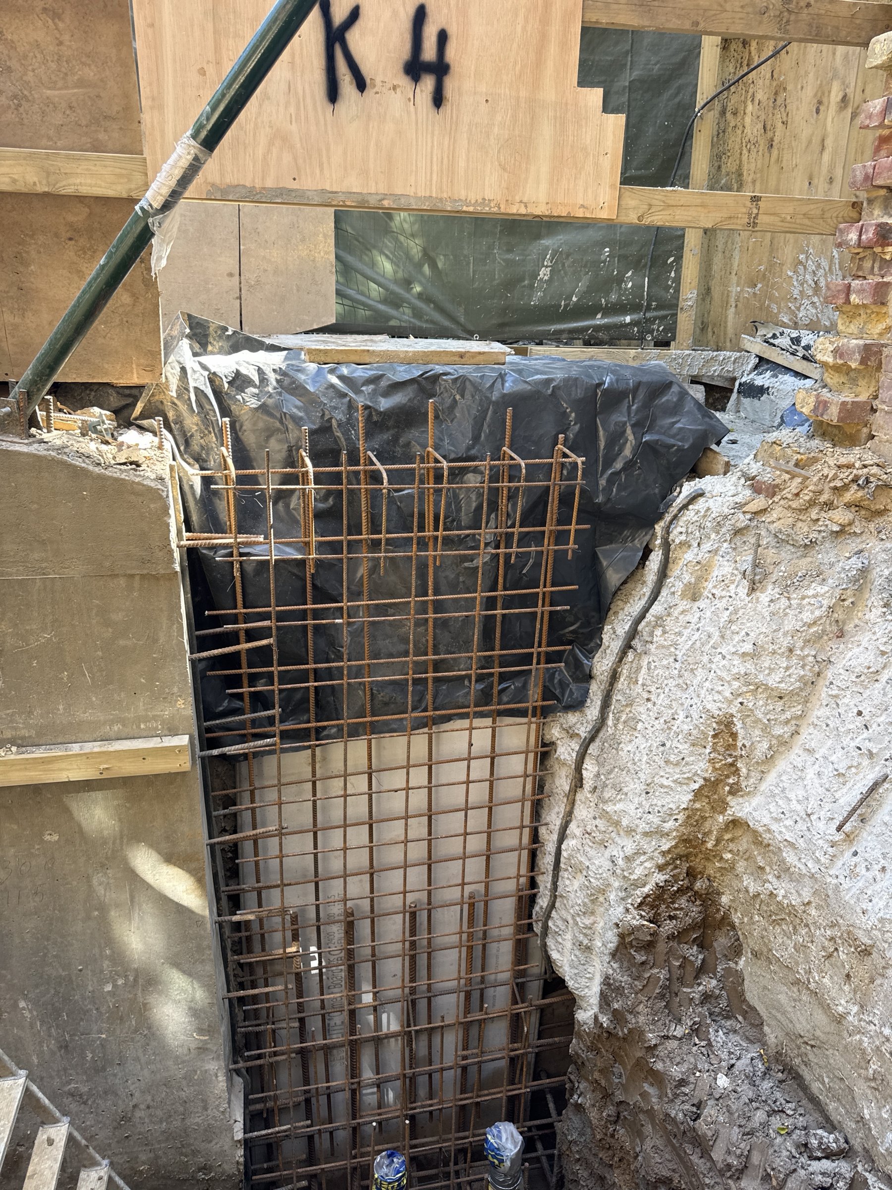 Reinforcement cage for underpinning pin K4 with damp proof membrane behind and the pin letter sprayed on the board above