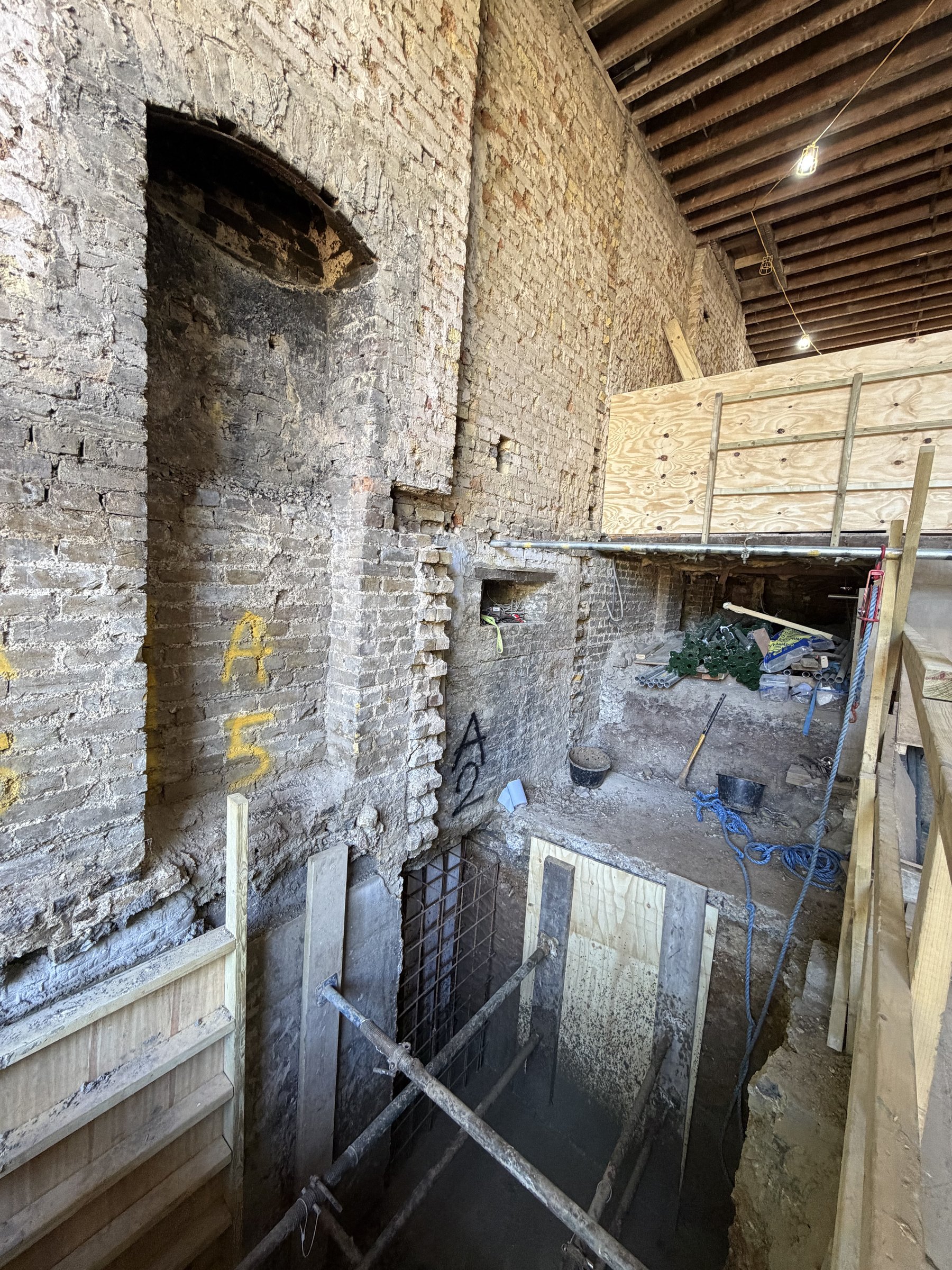 Old cellar wall with underpinning pins A2 and A5 marked in spray paint, shutters and props in the dig below